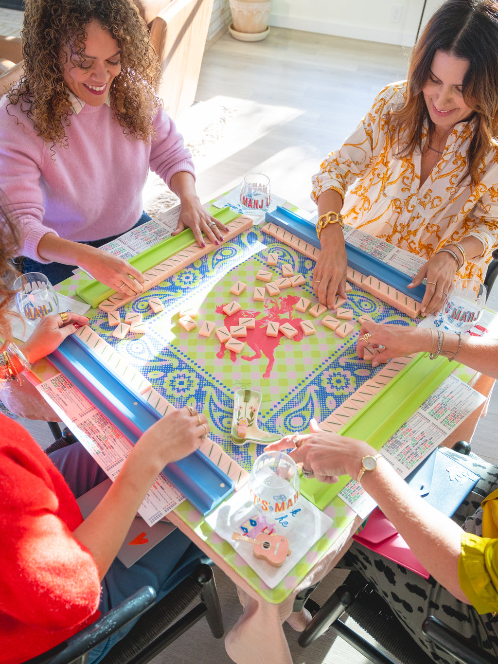Four people gathered around a colorful board game table, playing a game with wooden tokens and cards in a bright indoor setting.