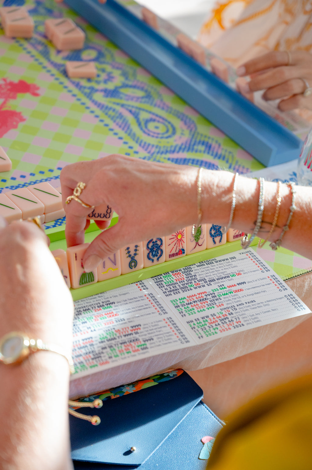 Close-up of a person's hands playing a colorful board game with wooden letter tiles and a printed game board in bright natural light.