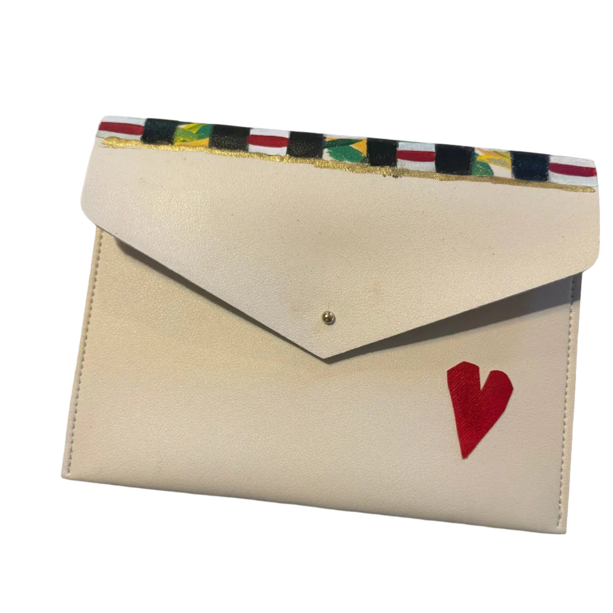 A cream-colored envelope-style wallet with a red heart on the front, placed on a light marble surface. The wallet has a colorful patterned strip along the top edge and is photographed with a pink hair clip and a small card visible in the background.