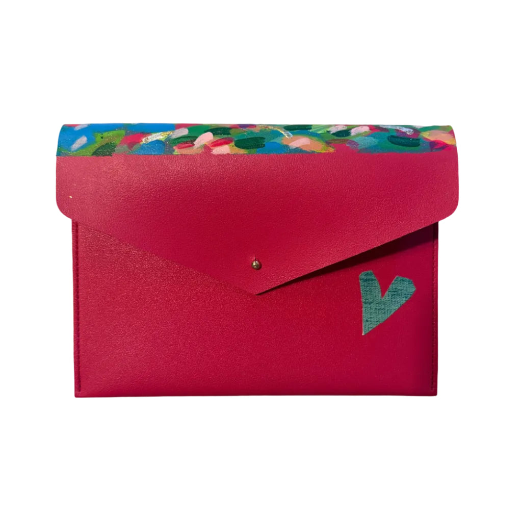 A bright pink envelope-style pouch with a colorful floral patterned top border and a small green heart detail on the front, photographed on a light marble surface.