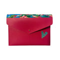 A bright pink envelope-style pouch with a colorful floral patterned top border and a small green heart detail on the front, photographed on a light marble surface.