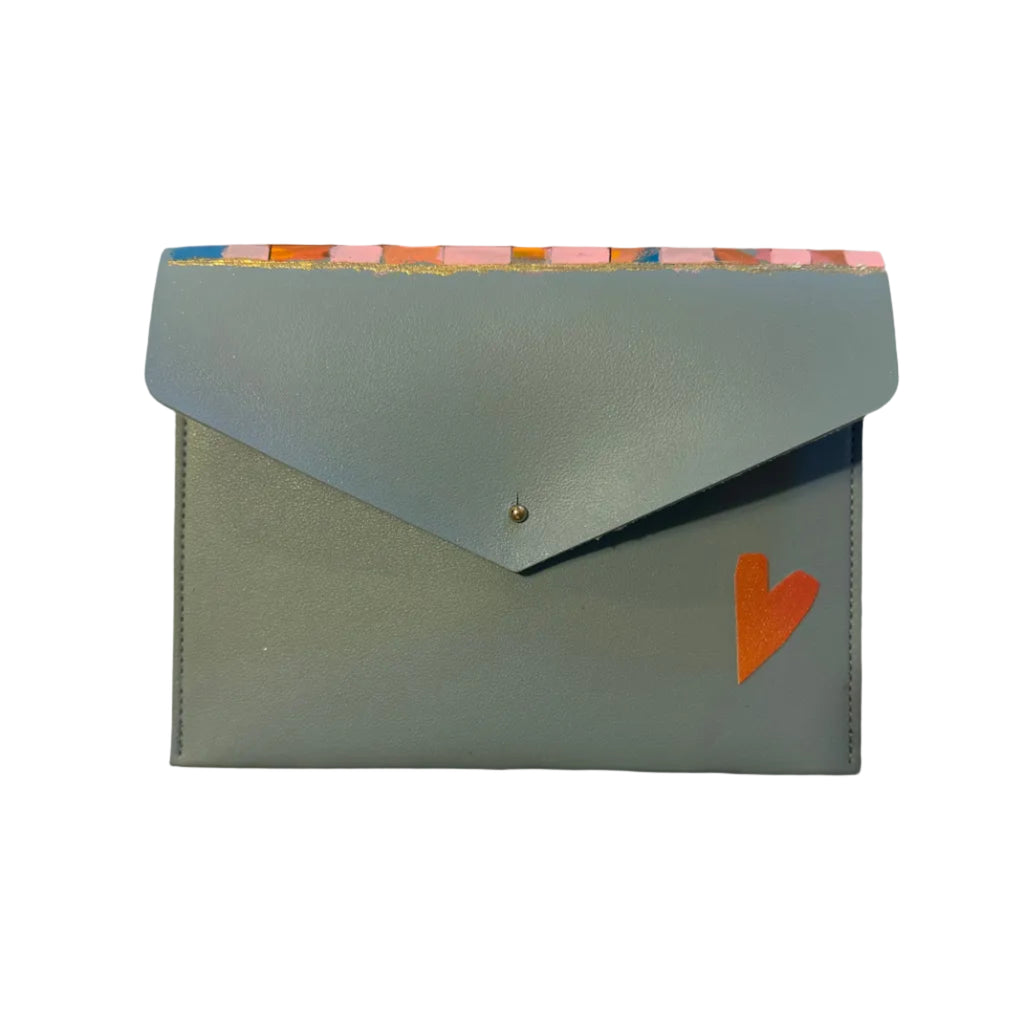 A light blue envelope-style card holder or small pouch with a flap closure, placed on a white marble surface. The flap has a small gold button, a small orange heart detail, and a colorful striped pattern along the top edge.