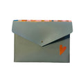 A light blue envelope-style card holder or small pouch with a flap closure, placed on a white marble surface. The flap has a small gold button, a small orange heart detail, and a colorful striped pattern along the top edge.