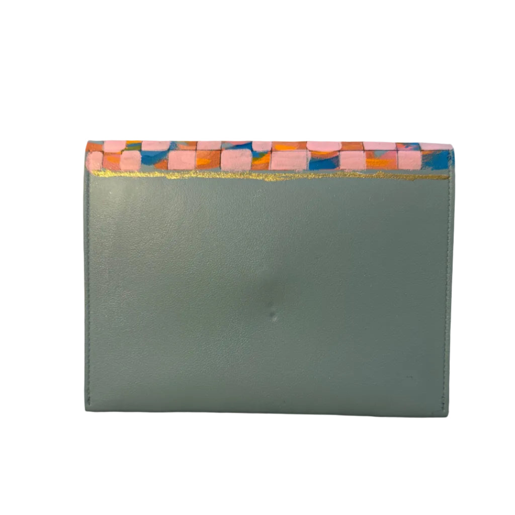 A sage green leather card holder or wallet with a colorful patterned paper trim along the top edge, resting on a white marble surface.