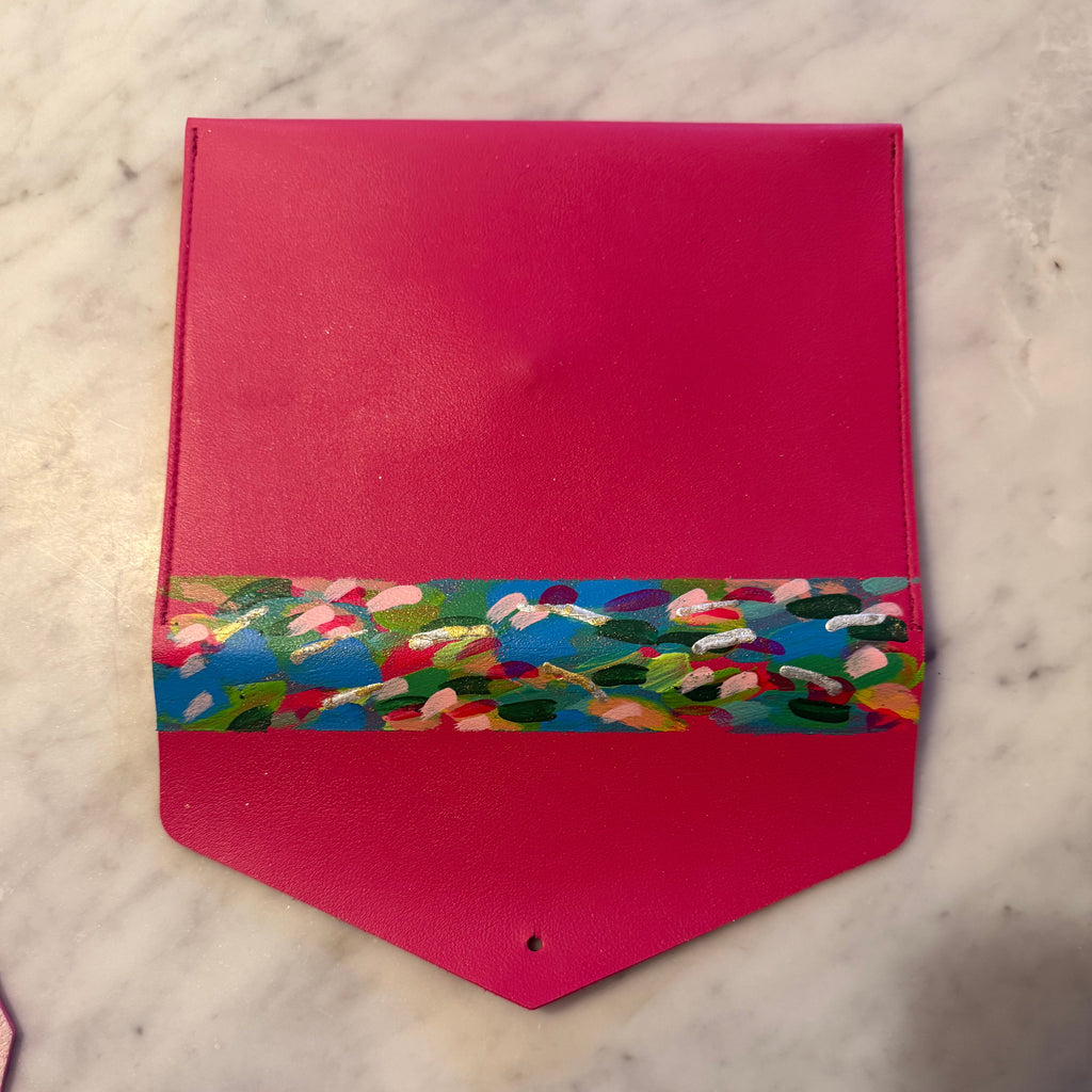 A bright pink leather pouch with a colorful floral patterned band around the middle, resting on a white marble surface.