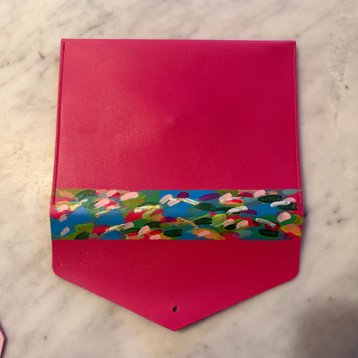 A bright pink leather pouch with a colorful floral patterned band around the middle, resting on a white marble surface.