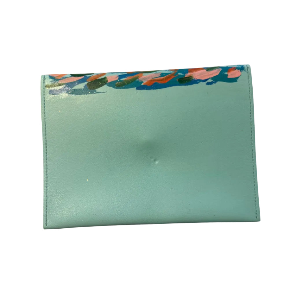 A mint green leather wallet with a colorful abstract patterned border on the top flap, resting on a white marble surface with a hand visible at the bottom.