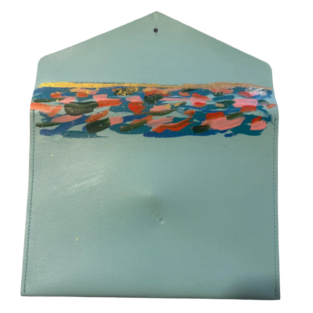 A mint blue leather envelope-style pouch with a colorful abstract painted stripe across the front, placed on a light marble surface.