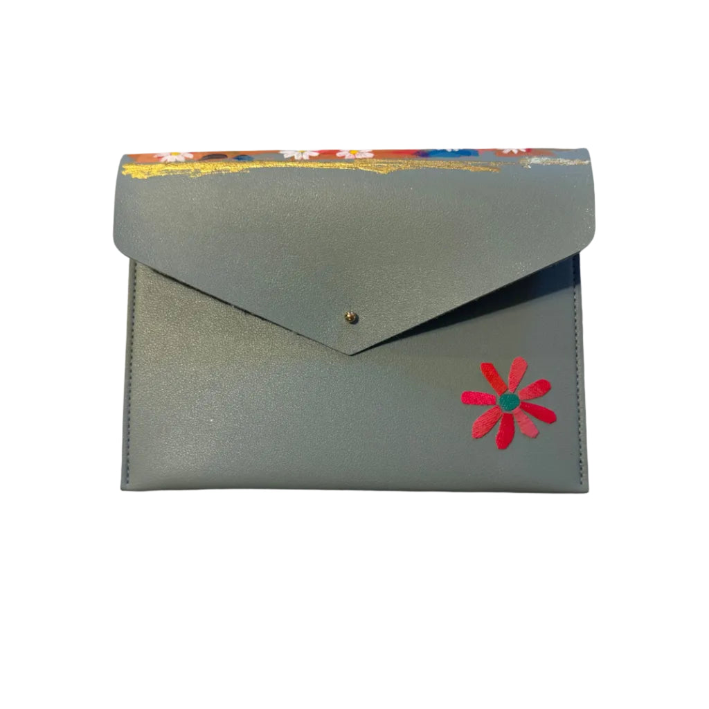 A small handmade envelope-style card holder or wallet in a muted dusty blue leather, decorated with a colorful painted top border and a pink flower applique on the front, resting on a white marble surface.