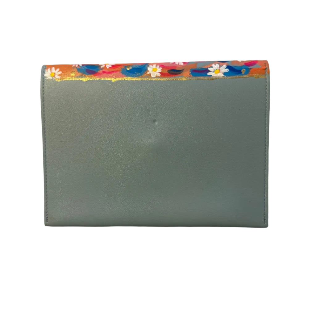 A dusty blue leather wallet with a colorful floral patterned top border, resting on a white marble surface.