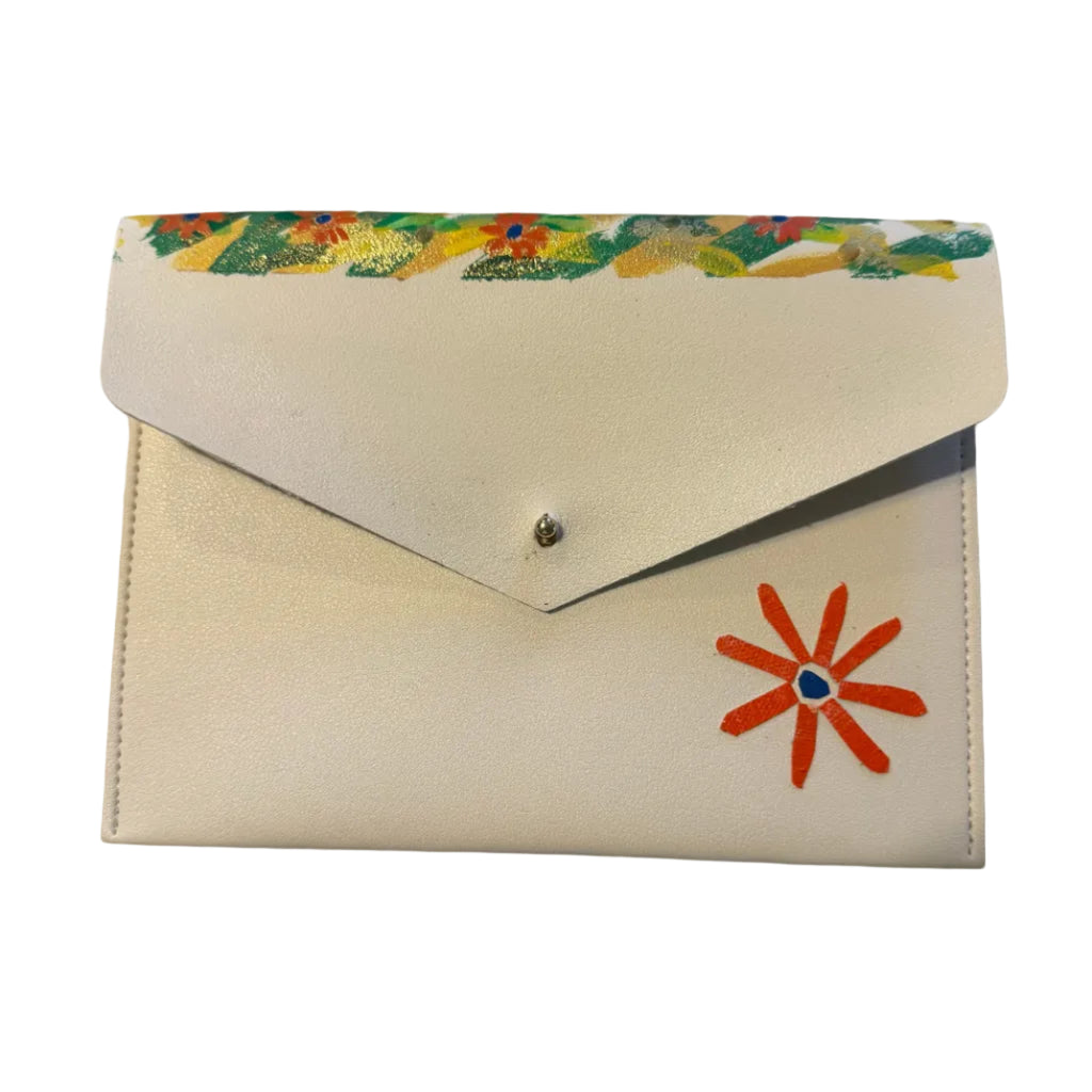A cream-colored envelope-style clutch wallet with a colorful floral pattern along the top flap edge and a red-orange flower applique on the front, resting on a white marble surface.