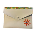 A cream-colored envelope-style clutch wallet with a colorful floral pattern along the top flap edge and a red-orange flower applique on the front, resting on a white marble surface.
