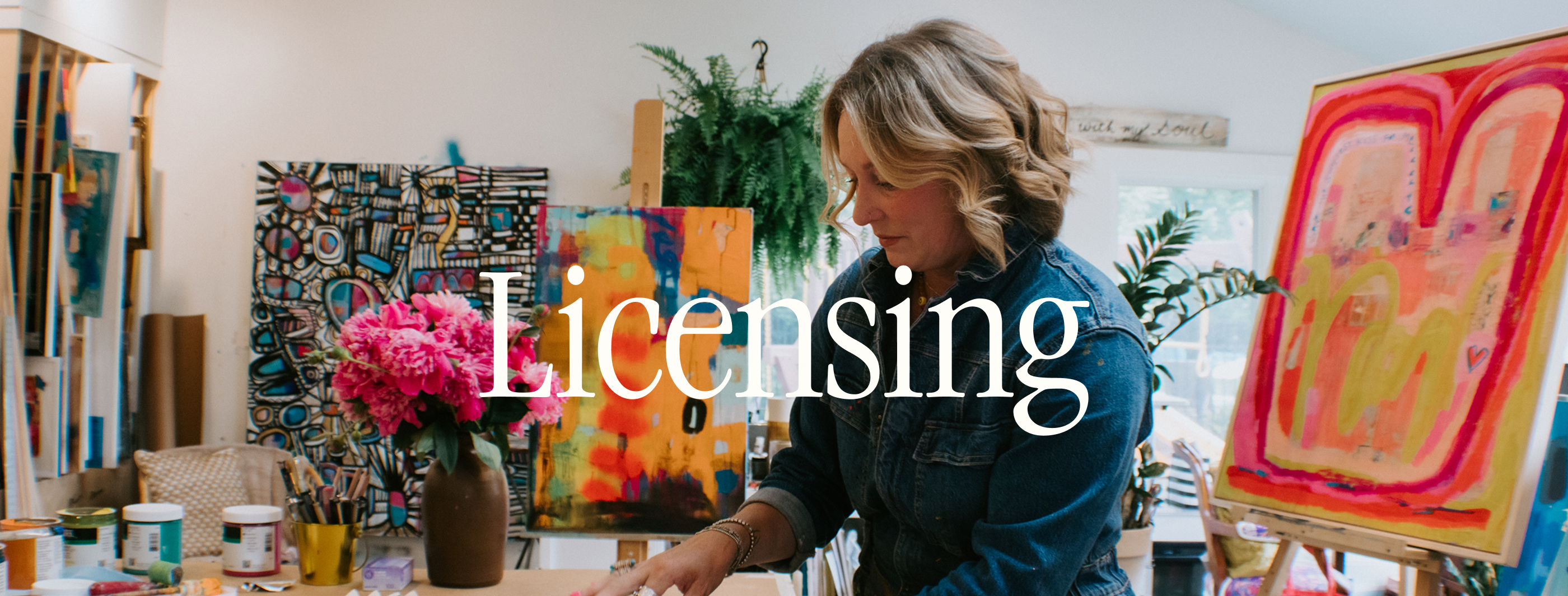 A woman in a denim jacket stands in a bright artist studio surrounded by colorful paintings, with a large white serif text overlay reading 'Licensing'.